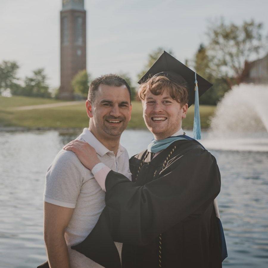 Luke Madden embracing someone while wearing his cap and gown, with the Cook Carillon clocktower in the background